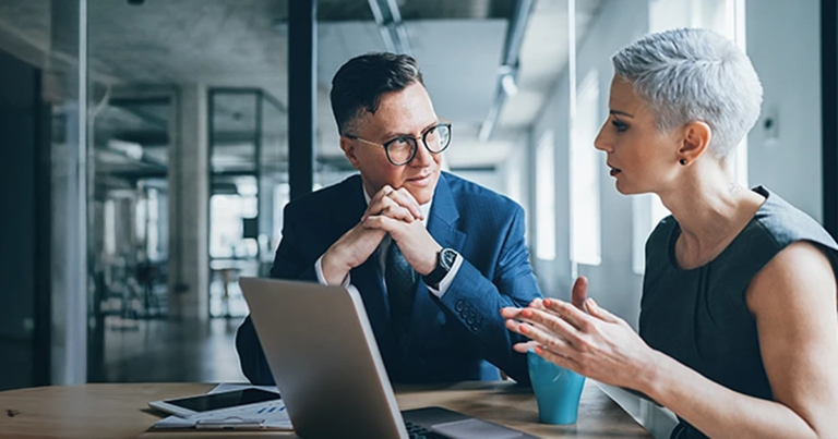 Geschäftsfrau mit kurzen Haaren und Geschäftsmann im Anzug diskutieren konstruktiv vor einem Computer. Erfolgreiches Konfliktmanagement