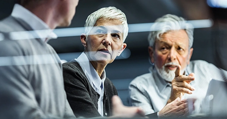 Gruppe im intensiven Austausch, Handgestik sichtbar, reflektierende Glasflächen betonen die sachliche Atmosphäre. Strategic Mind – Strategisch Denken