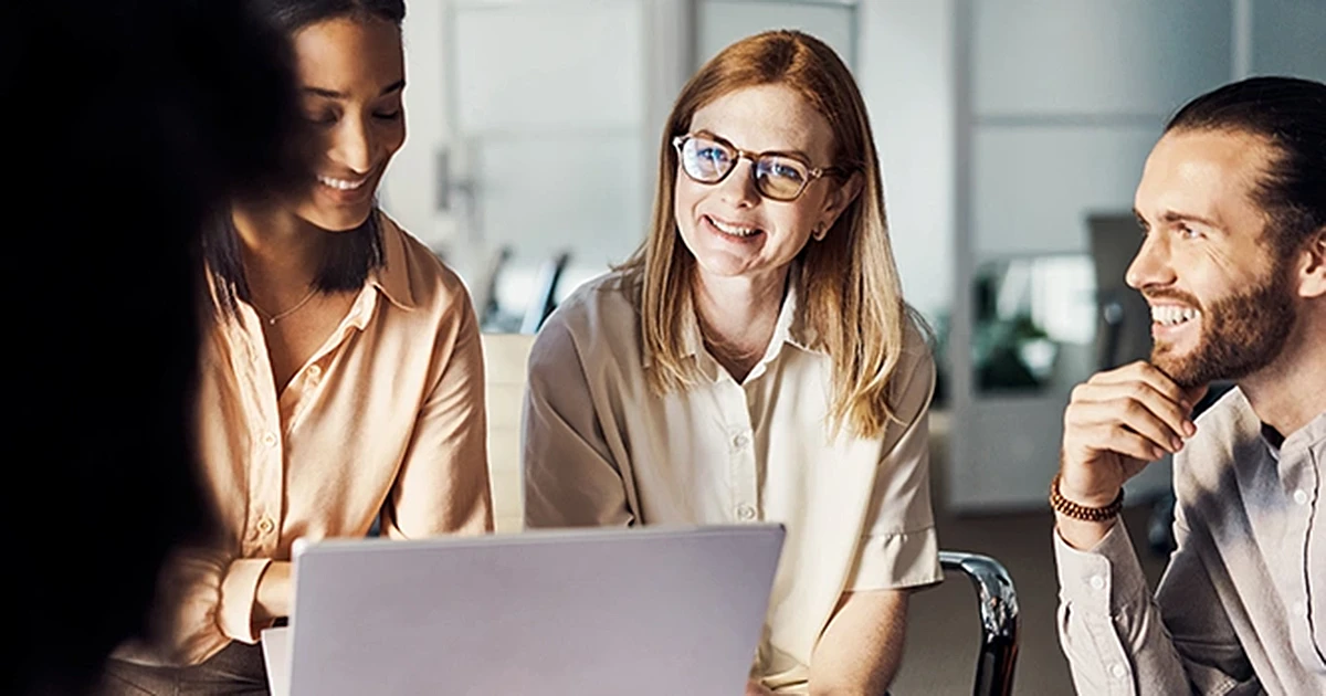 Zwei Frauen und ein Mann sitzen lächelnd vor einem aufgeklappten Laptop und besprechen Inhalte, helles Büro im Hintergrund. Grundlagen für eine Vertriebsstrategie