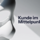 Abstrakte 3D-Skulptur auf hellem Hintergrund mit dem schwarzen Schriftzug „Kunde im Mittelpunkt". Customer Centricity