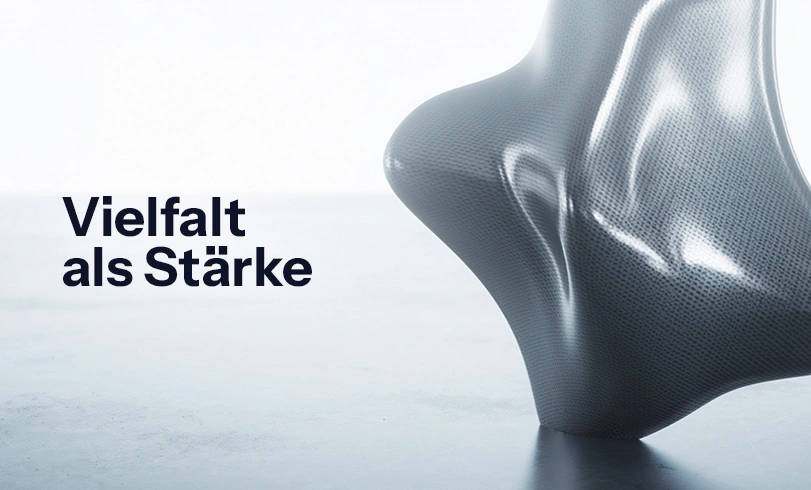 blog-diversitaet-im-unternehmen Abstrakte 3D-Skulptur auf hellem Hintergrund mit dem schwarzen Schriftzug „Vielfalt als Stärke". Diversität